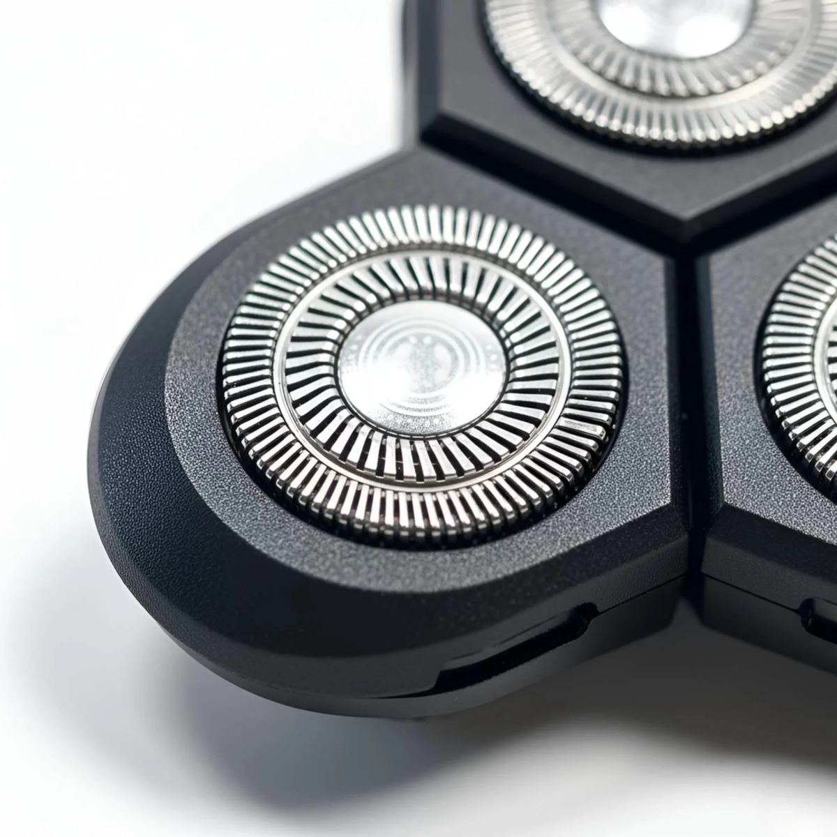 Close-up of a black rotary electric shaver head showing three circular silver metallic shaving nozzles on a white background.